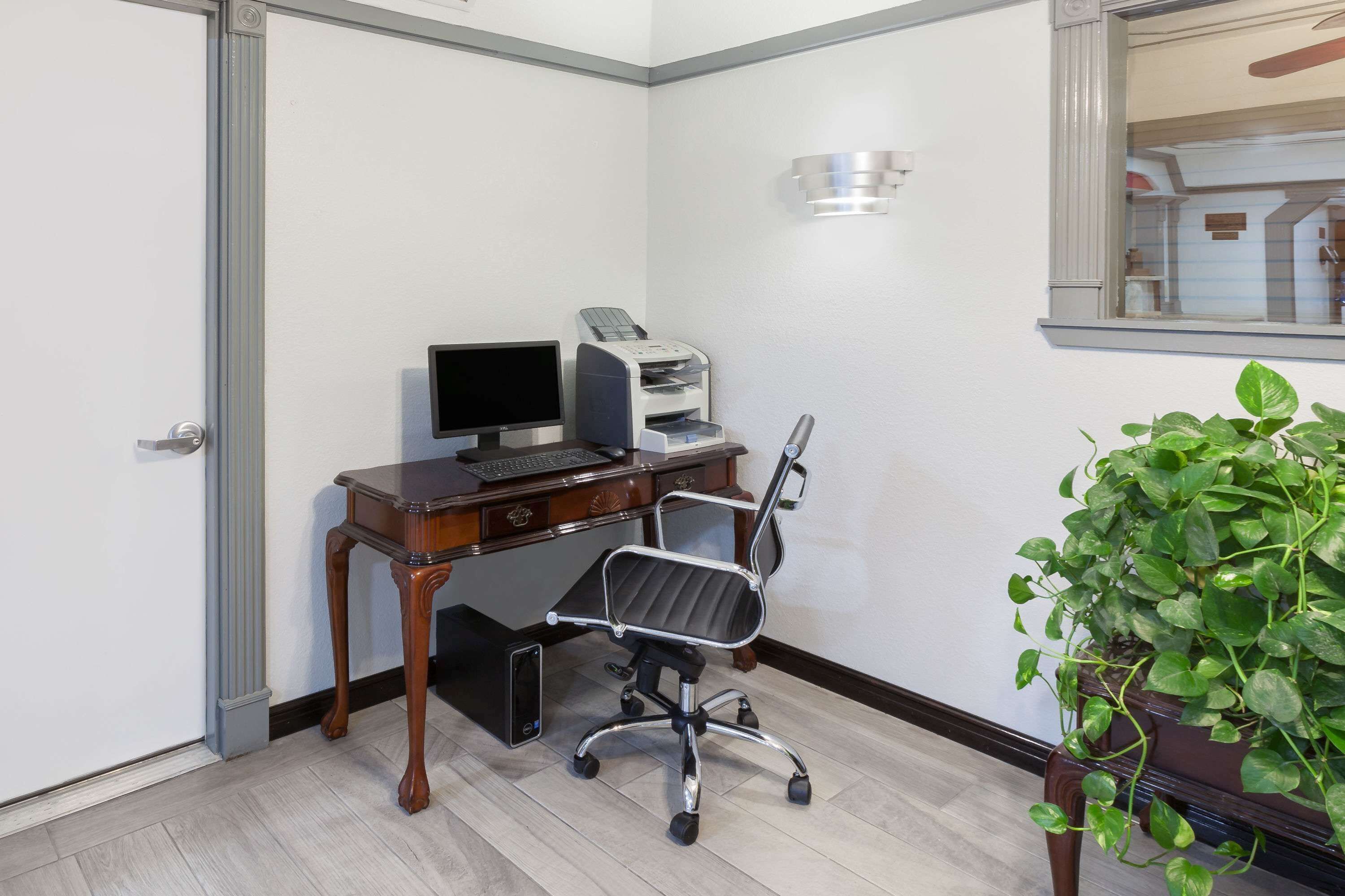 A small office space with a wooden desk, a computer, a printer, and a potted plant.