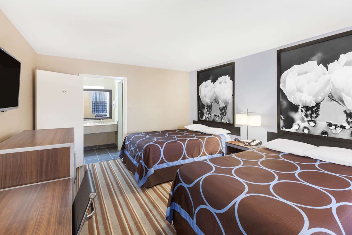 A hotel room with two beds, a desk, a TV, and artwork on the walls.