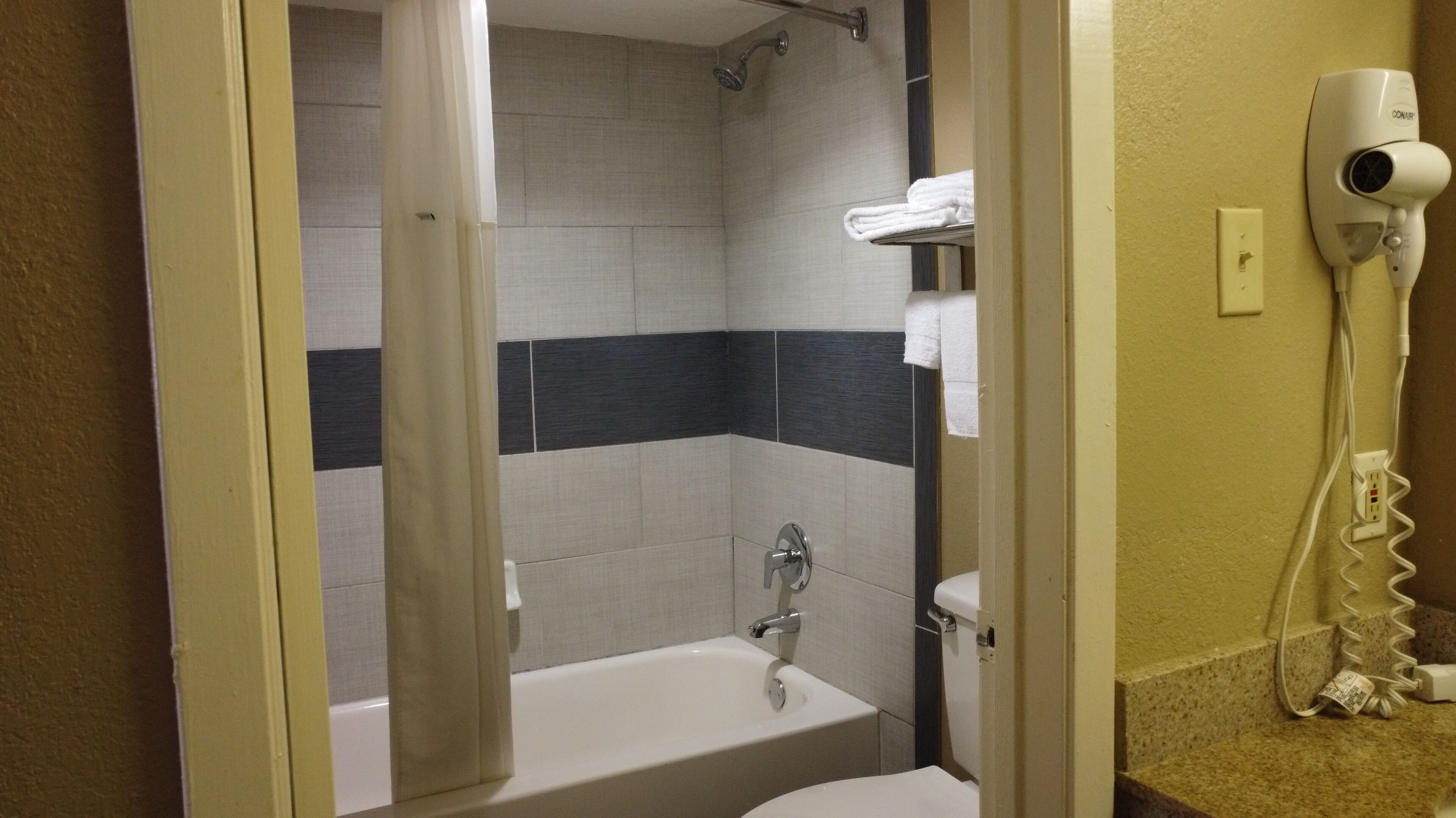 A bathroom with a bathtub, a shower, and a hairdryer on the wall.