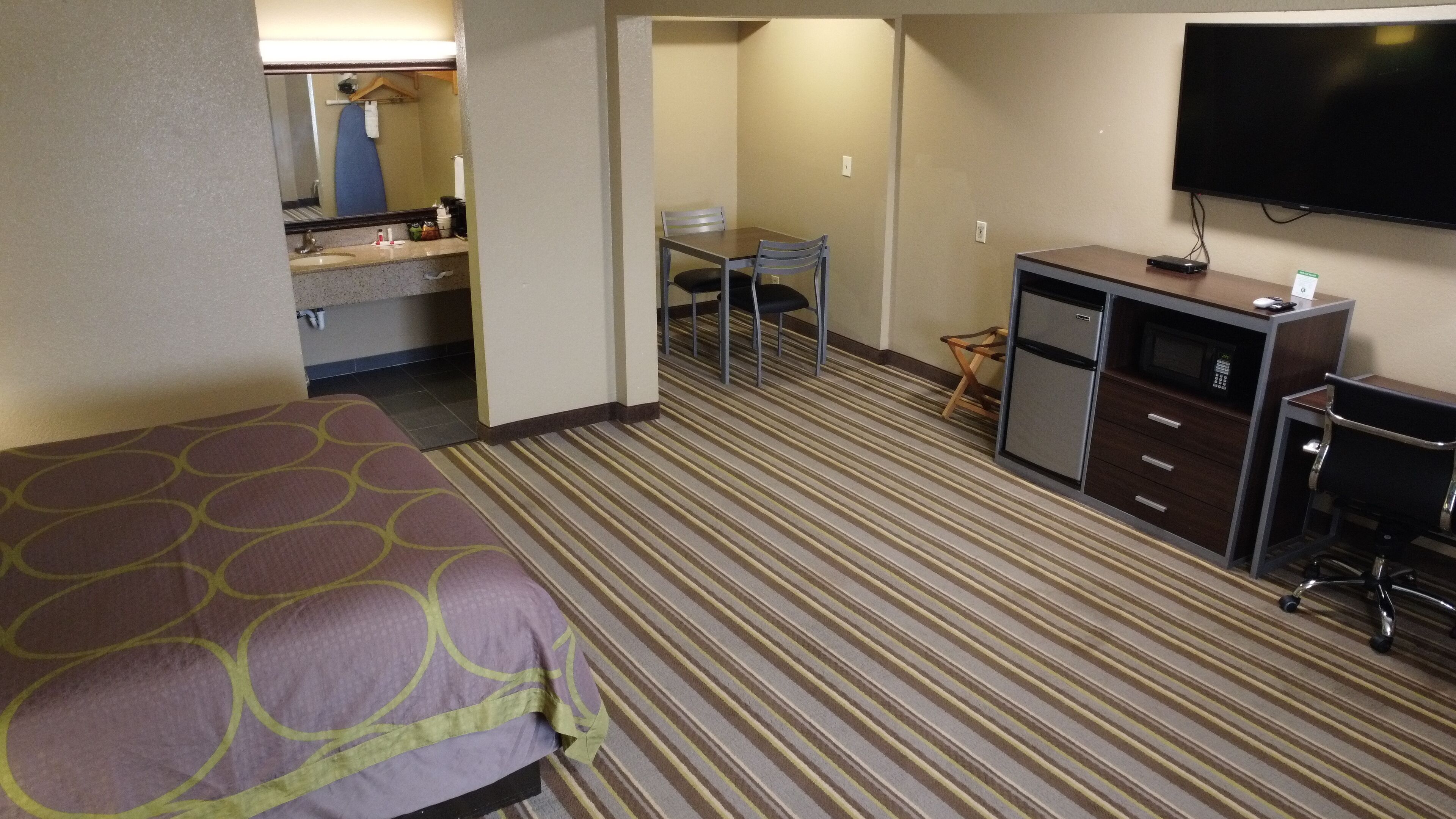 Habitación de hotel con una cama, un escritorio con computadora, televisor y baño con lavamanos y espejo.