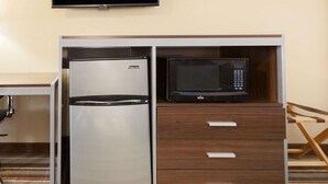 A compact kitchenette with a refrigerator and microwave, a wooden cabinet with drawers, and a television mounted on the wall. - Super 8 by Wyndham Kingsville (Kingsville)