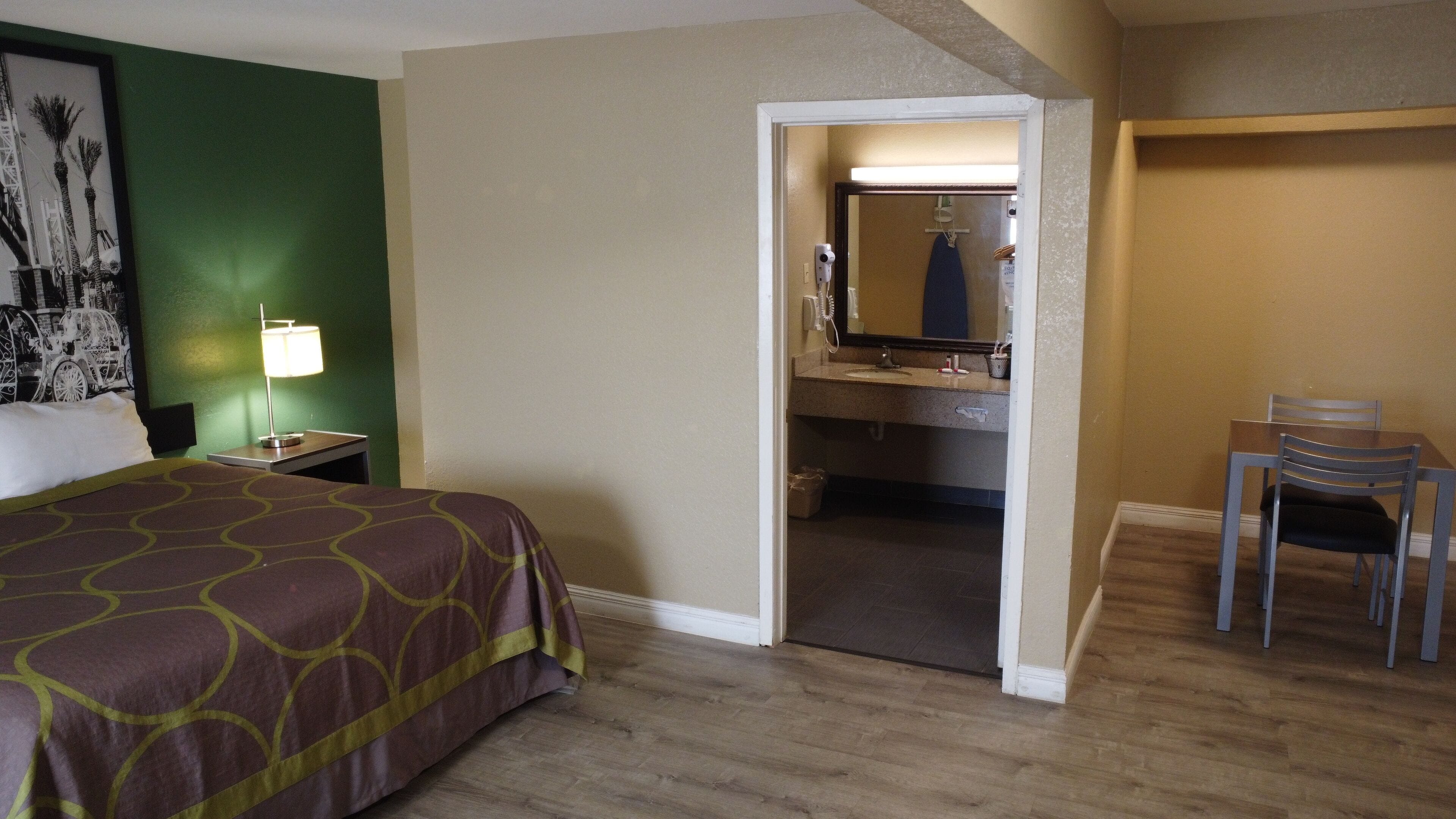 Hotelkamer met een bed, bureau, stoel, badkamer met spiegel en een groene wand met een afbeelding.