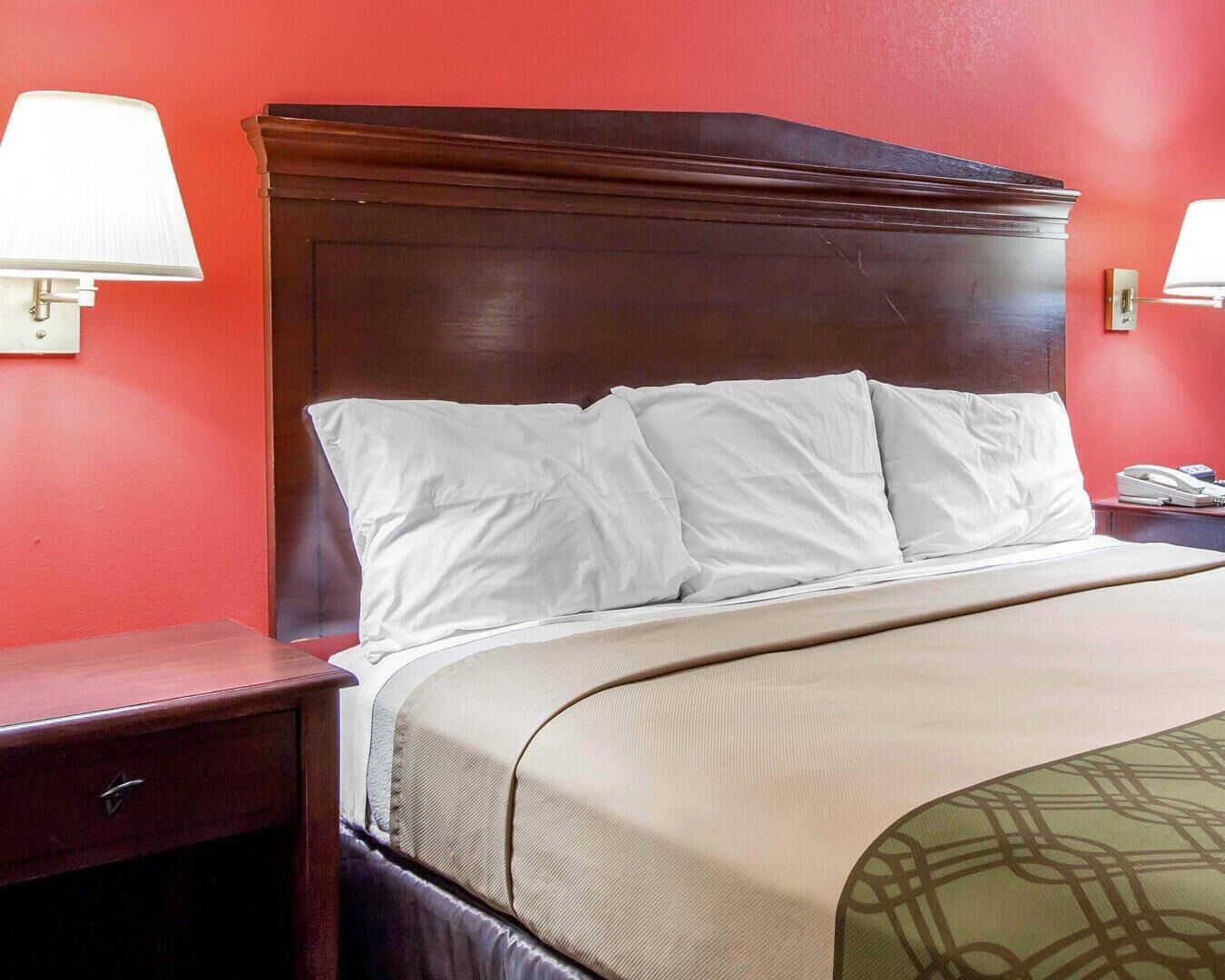 A hotel room with a wooden headboard, a bed with white bedding, a bedside table, and a lamp.