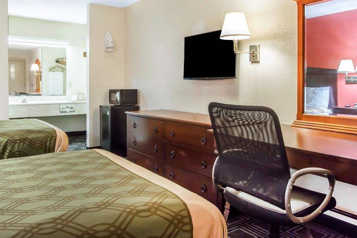 A hotel room with two beds, a dresser, a television, and a mirror.