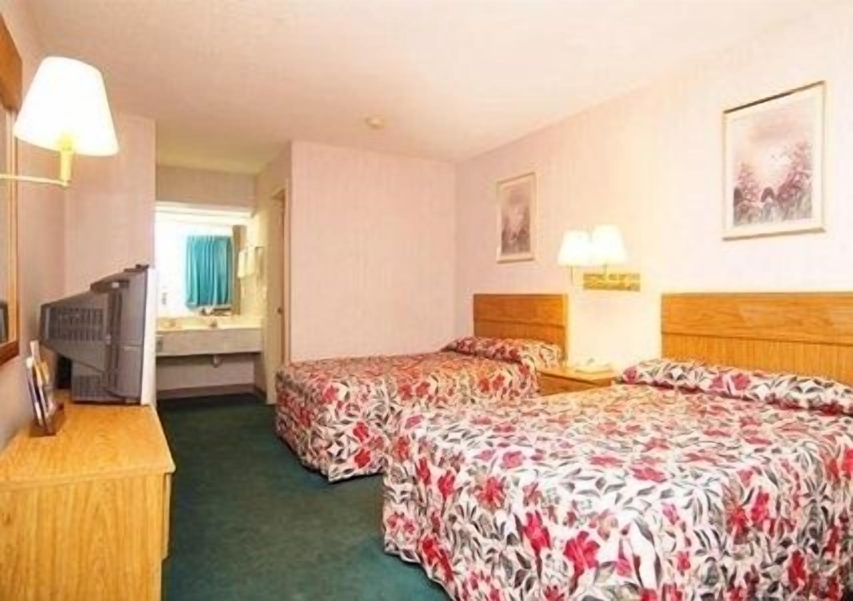 A hotel room with two beds, a wooden headboard, a nightstand, a lamp, and a mirror.