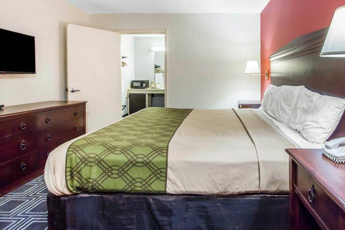 A hotel room with a bed, a dresser, a television, a desk with a mirror, and a lamp.