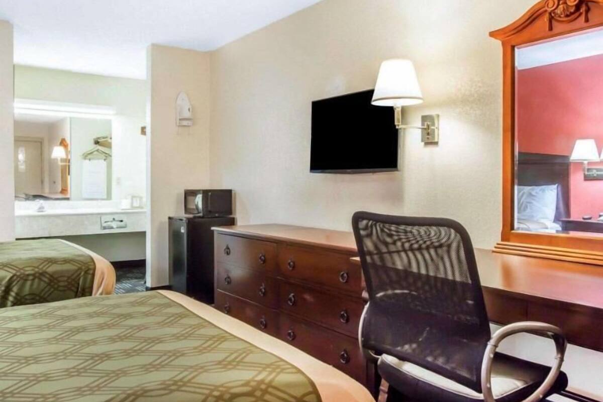A hotel room with two beds, a dresser, a chair, a television, and a mirror.
