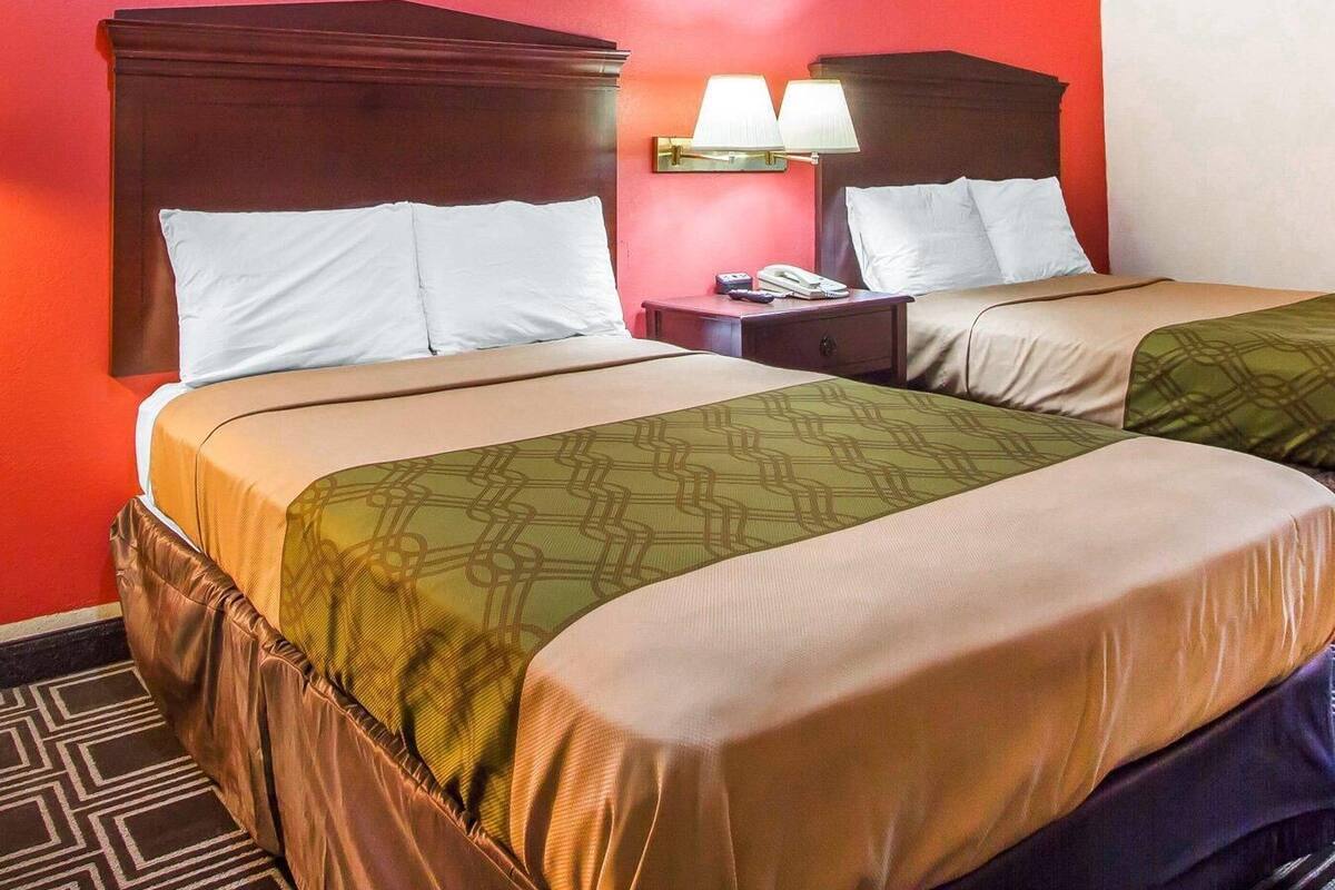 A hotel room with two beds, a nightstand with a lamp, and a telephone.