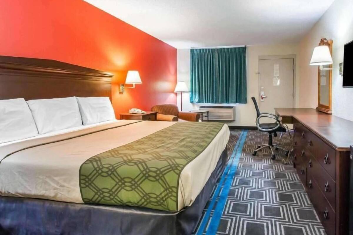A hotel room with a bed, a desk, a chair, a dresser, and a window with curtains.