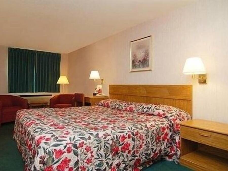 A hotel room with a bed, two bedside tables, a chair, and a window with curtains.