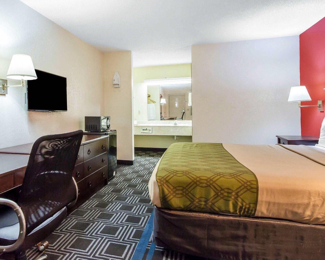 A hotel room with a bed, desk, chair, television, and a bathroom visible through an open door.