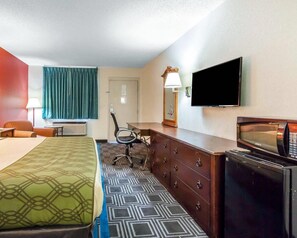 Habitación de hotel con cama, escritorio, silla, cómoda, televisor y ventana con cortinas.