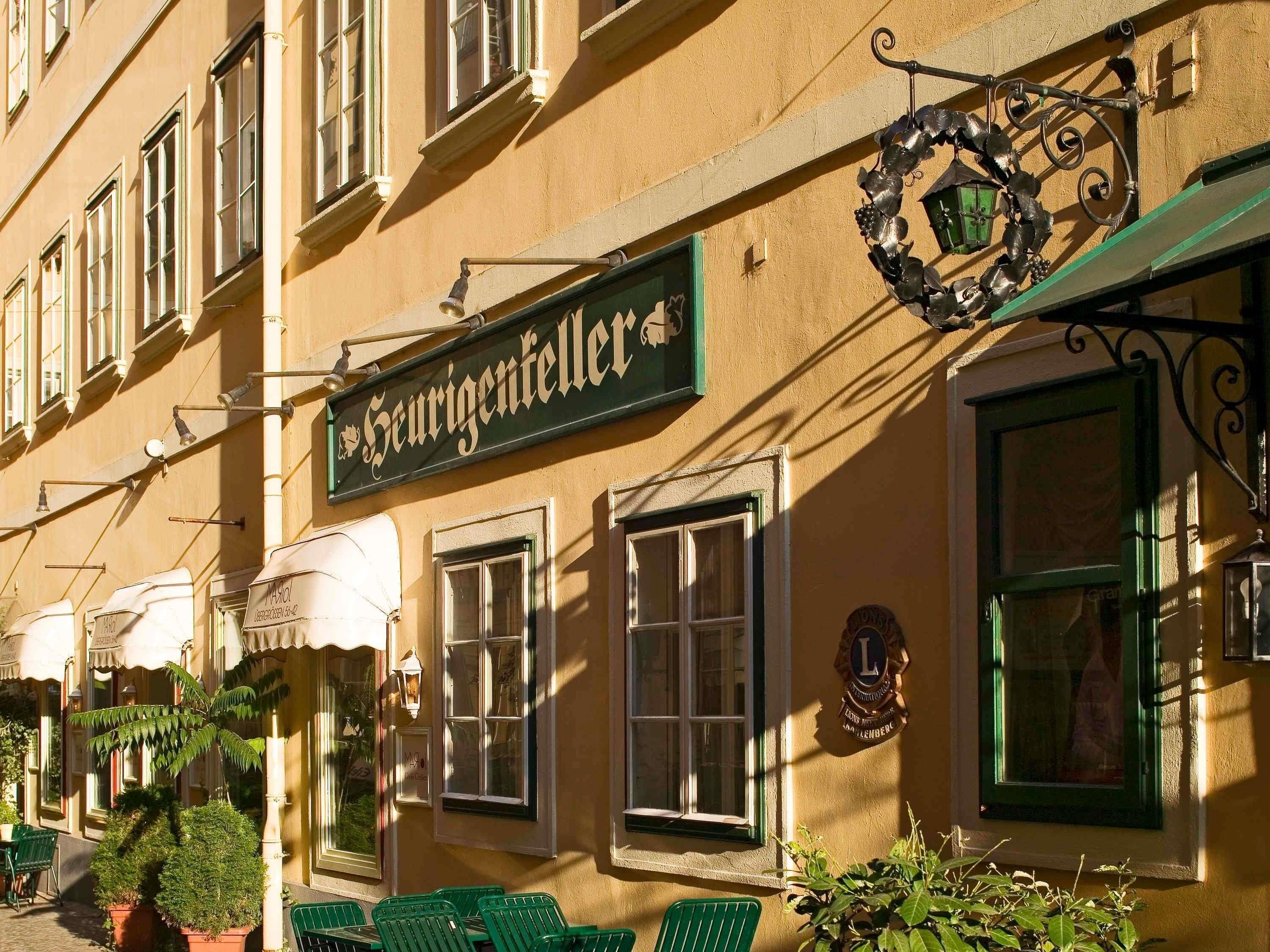 Um edifício com uma placa indicando 'Seurigenfeller', com várias janelas, área externa para sentar e uma placa de metal decorativa.