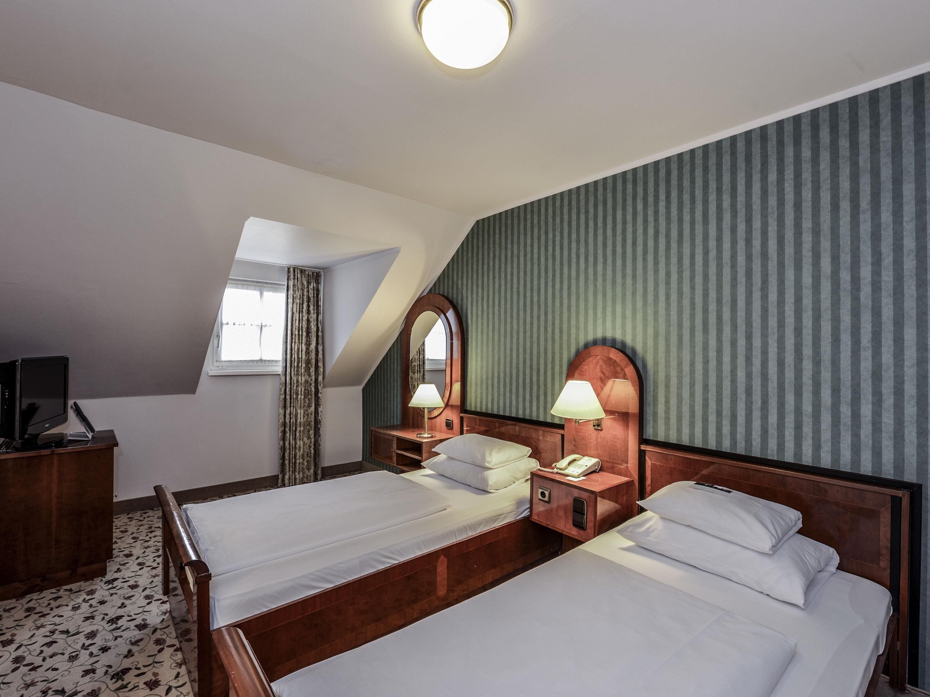 A hotel room with two beds, a desk with a computer, a telephone, and a mirror.