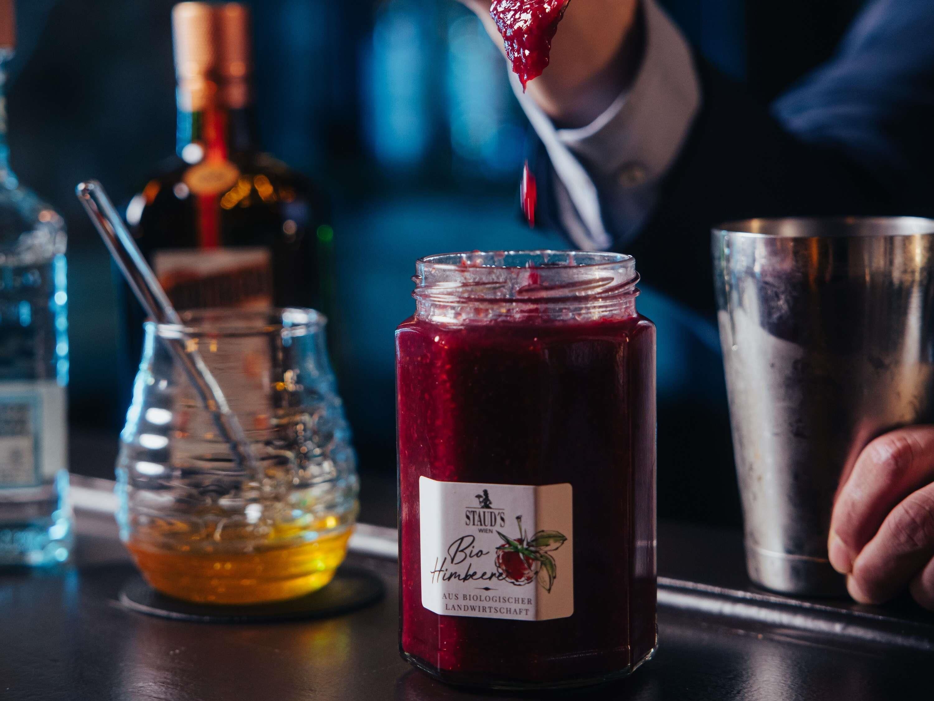 Um pote de Bio Himbeere, uma garrafa de vinho e um coqueteleira em um balcão de bar.