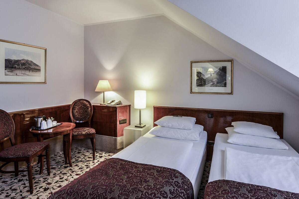 Ein Hotelzimmer mit zwei Betten, einem Schreibtisch mit Stuhl, einer Lampe und gerahmten Bildern an den Wänden.