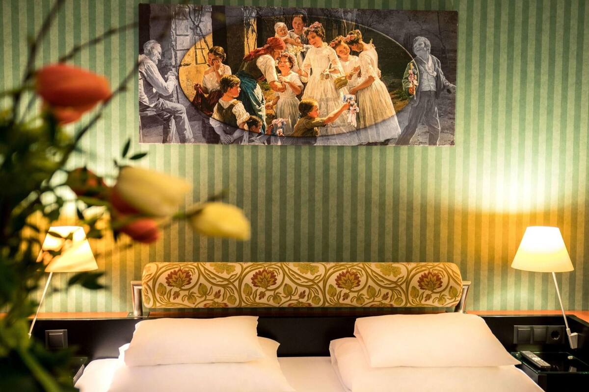 Ein Hotelzimmer mit einem Bett, zwei Nachttischlampen, einem blumengemusterten Kopfteil und einem großen Wandbild.