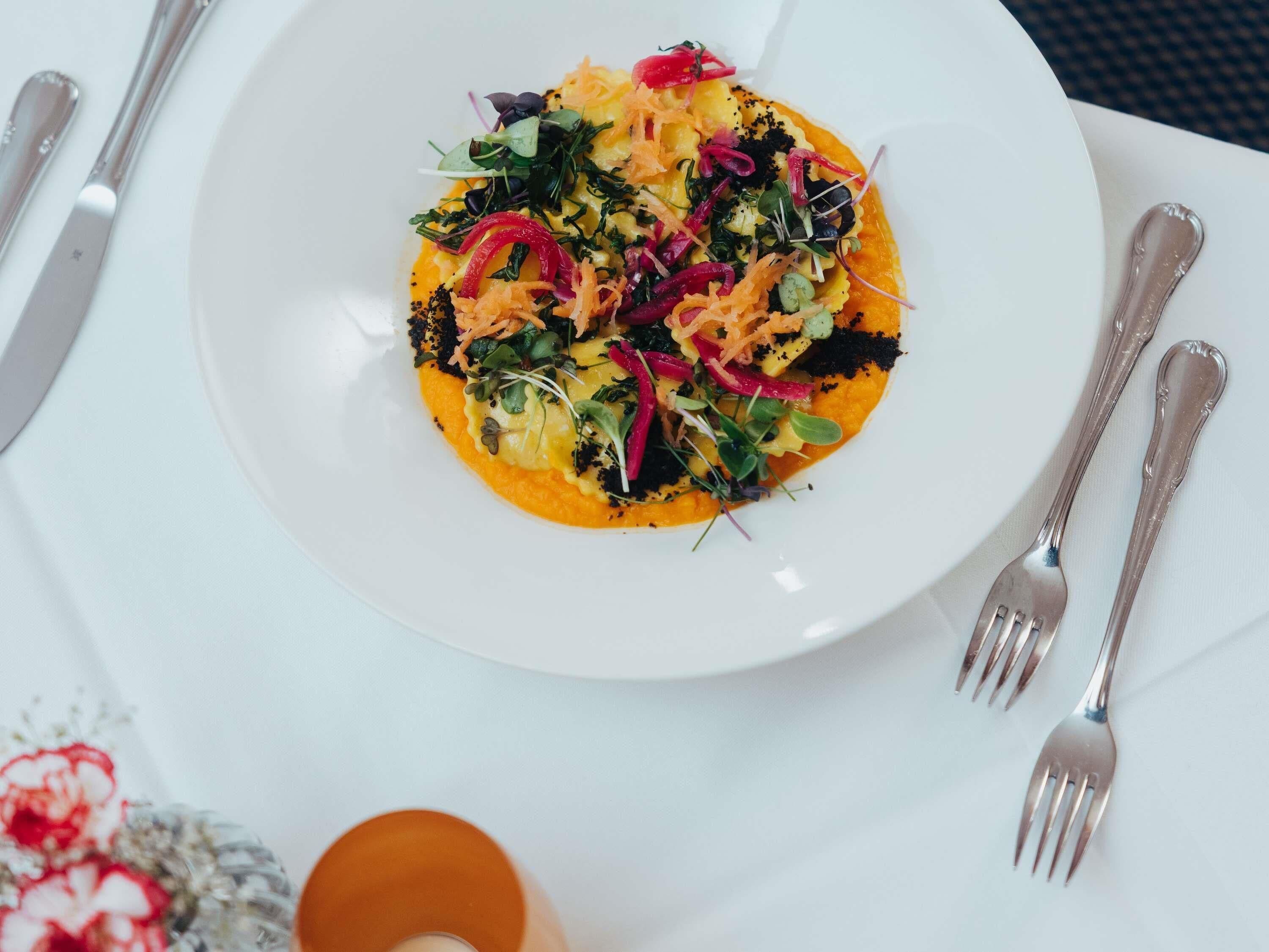 Um prato branco com um prato colorido, talheres de prata e uma toalha de mesa branca.