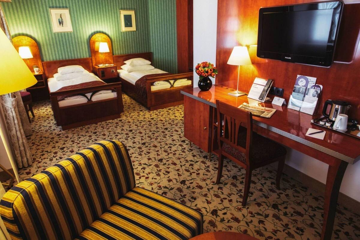 Ein Hotelzimmer mit zwei Betten, einem Schreibtisch, einem Flachbildfernseher, einer Couch und einer Kaffeemaschine.