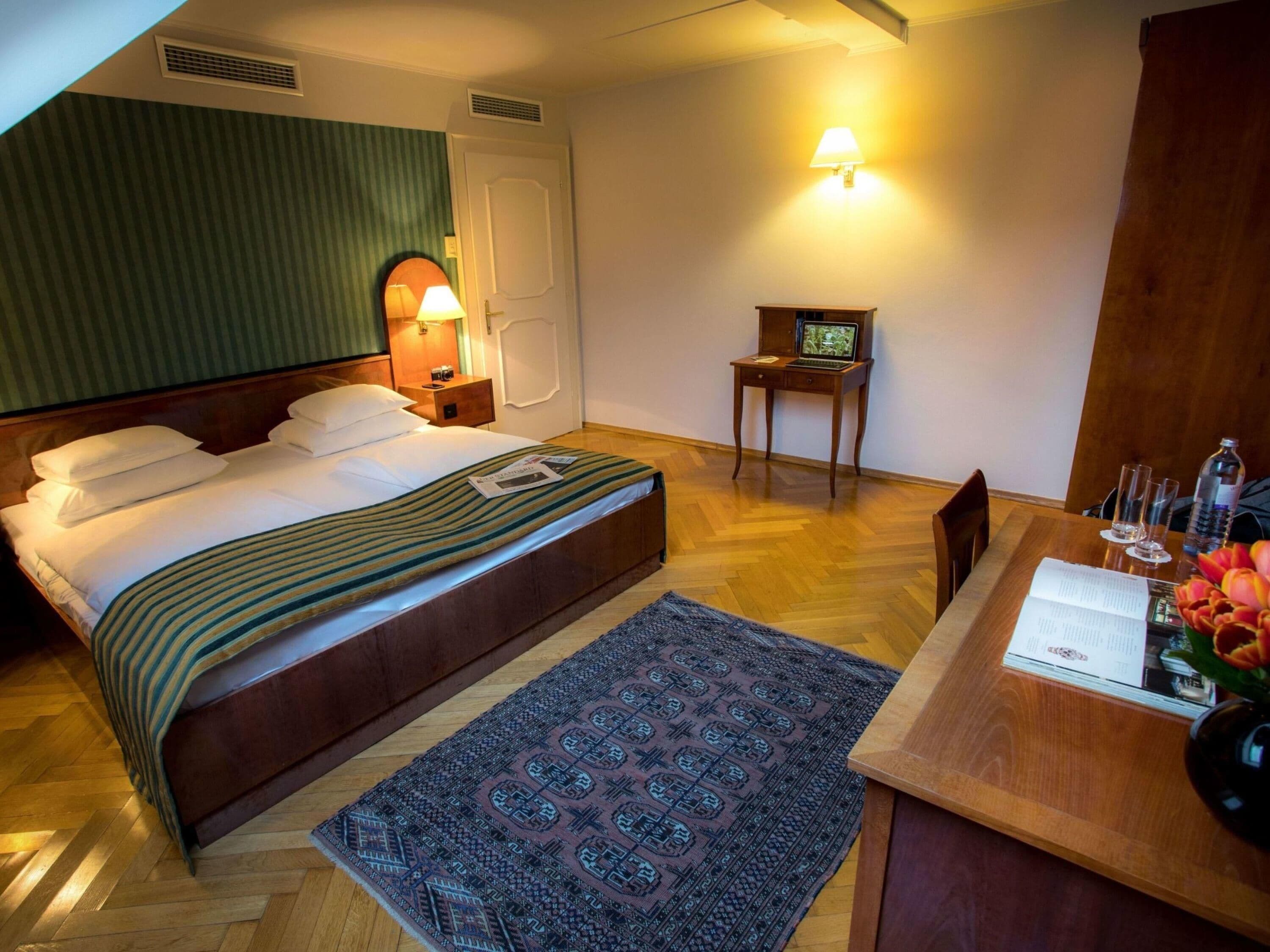 Habitación de hotel con cama, escritorio, silla, una mesita, lámpara y televisión instalada en la pared.