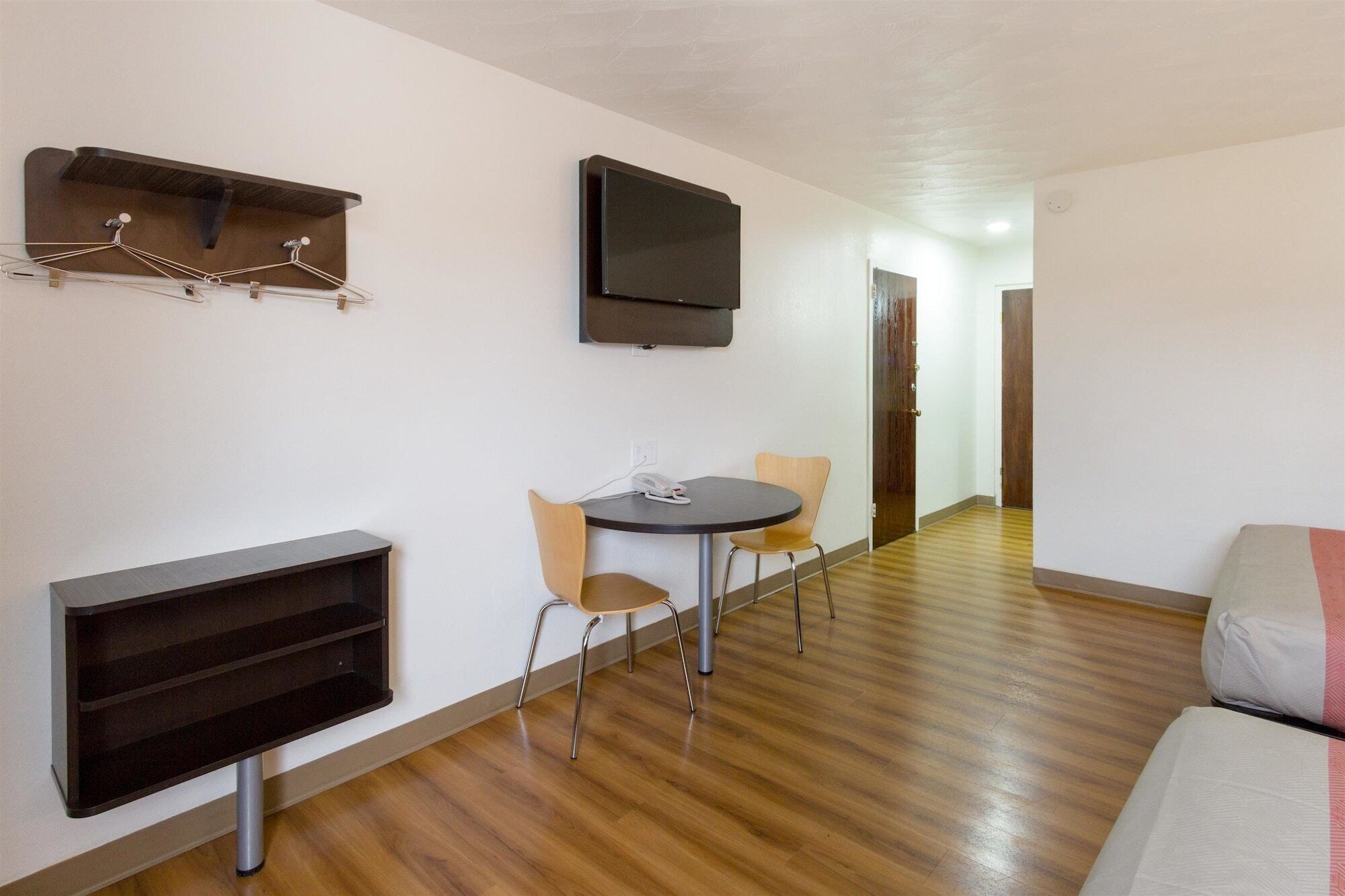 A compact living space with a flat-screen TV, a small dining table with chairs, a sofa, and a built-in shelf.