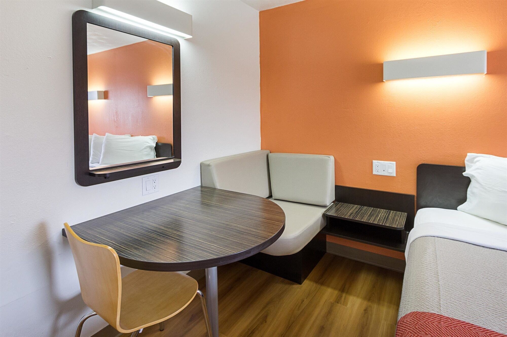A compact hotel room with a round table, a single chair, a sofa, and a bed.