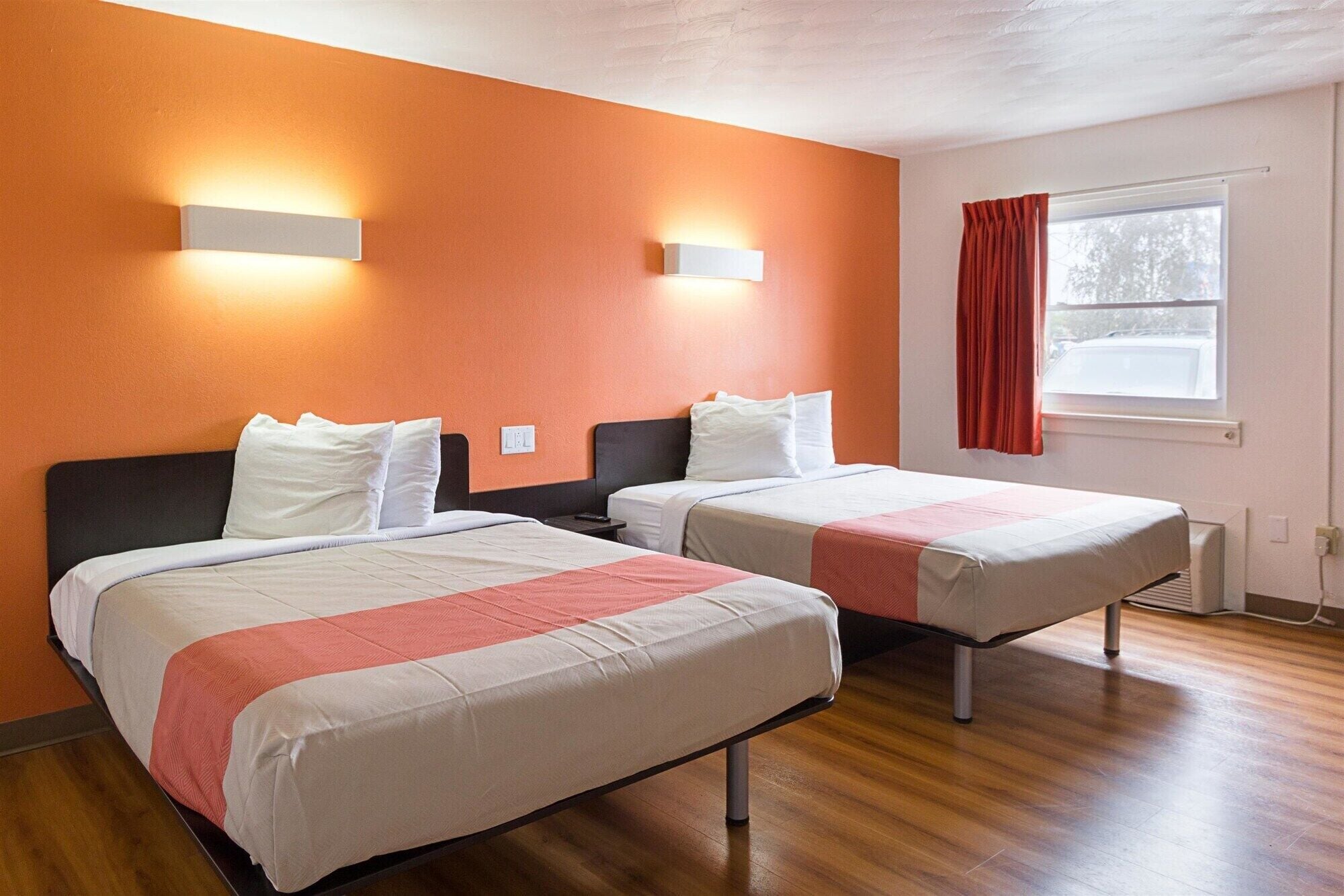 A hotel room with two beds, orange walls, and a window with a red curtain.