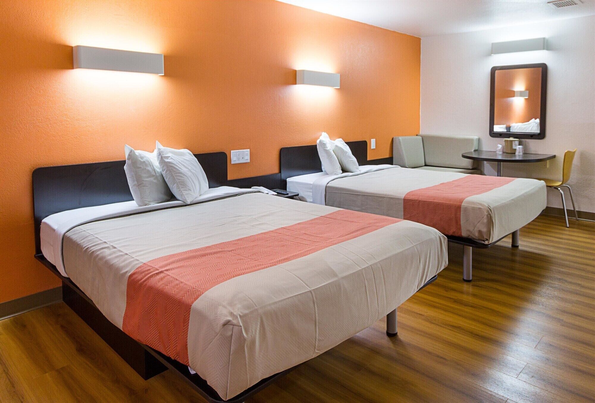 A hotel room with two beds, a small table, a chair, and a mirror on the wall.