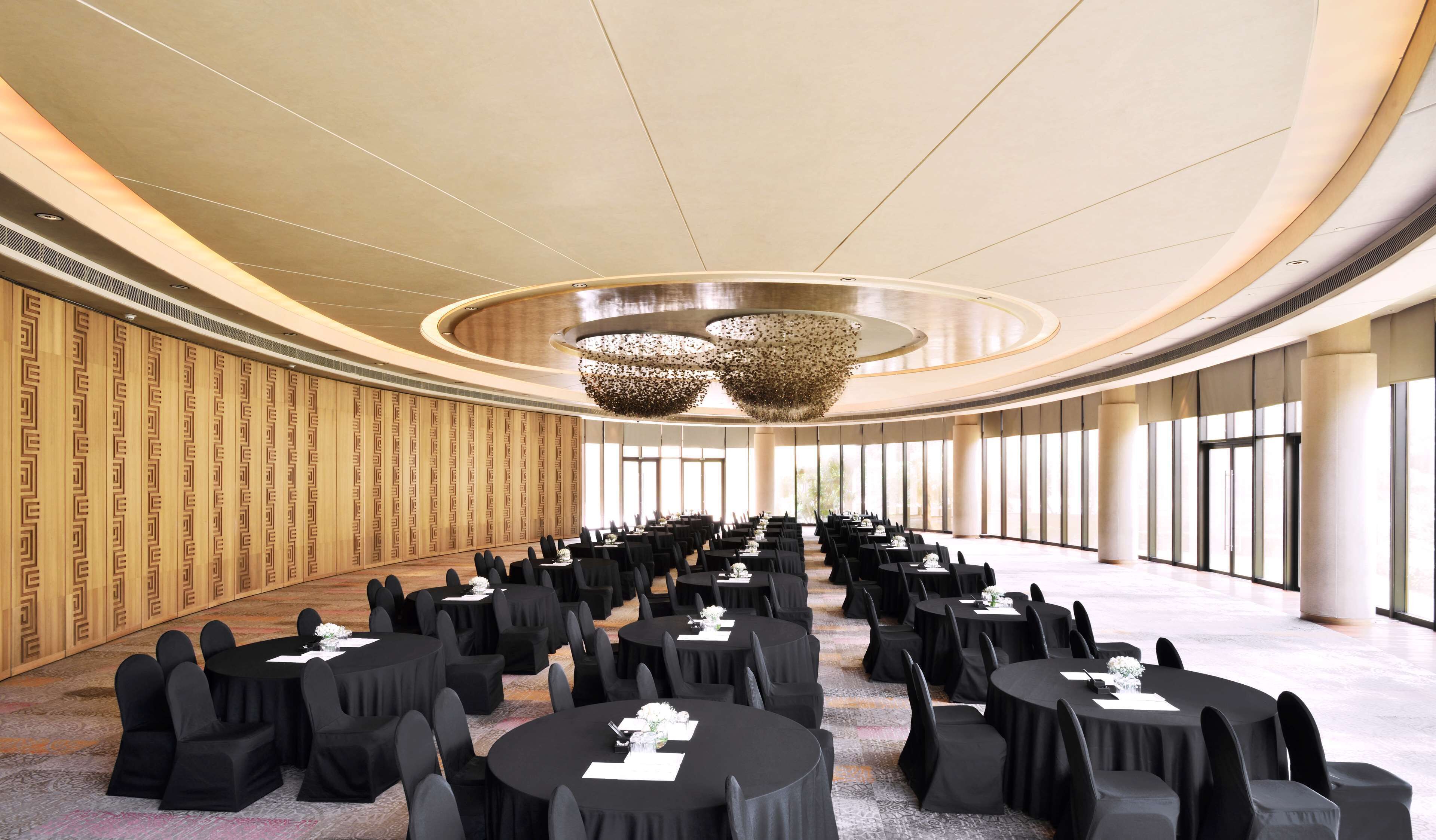 Un salón de conferencias amplio y bien iluminado, con mesas y sillas redondas, un diseño de pared con motivos y un diseño de techo moderno.