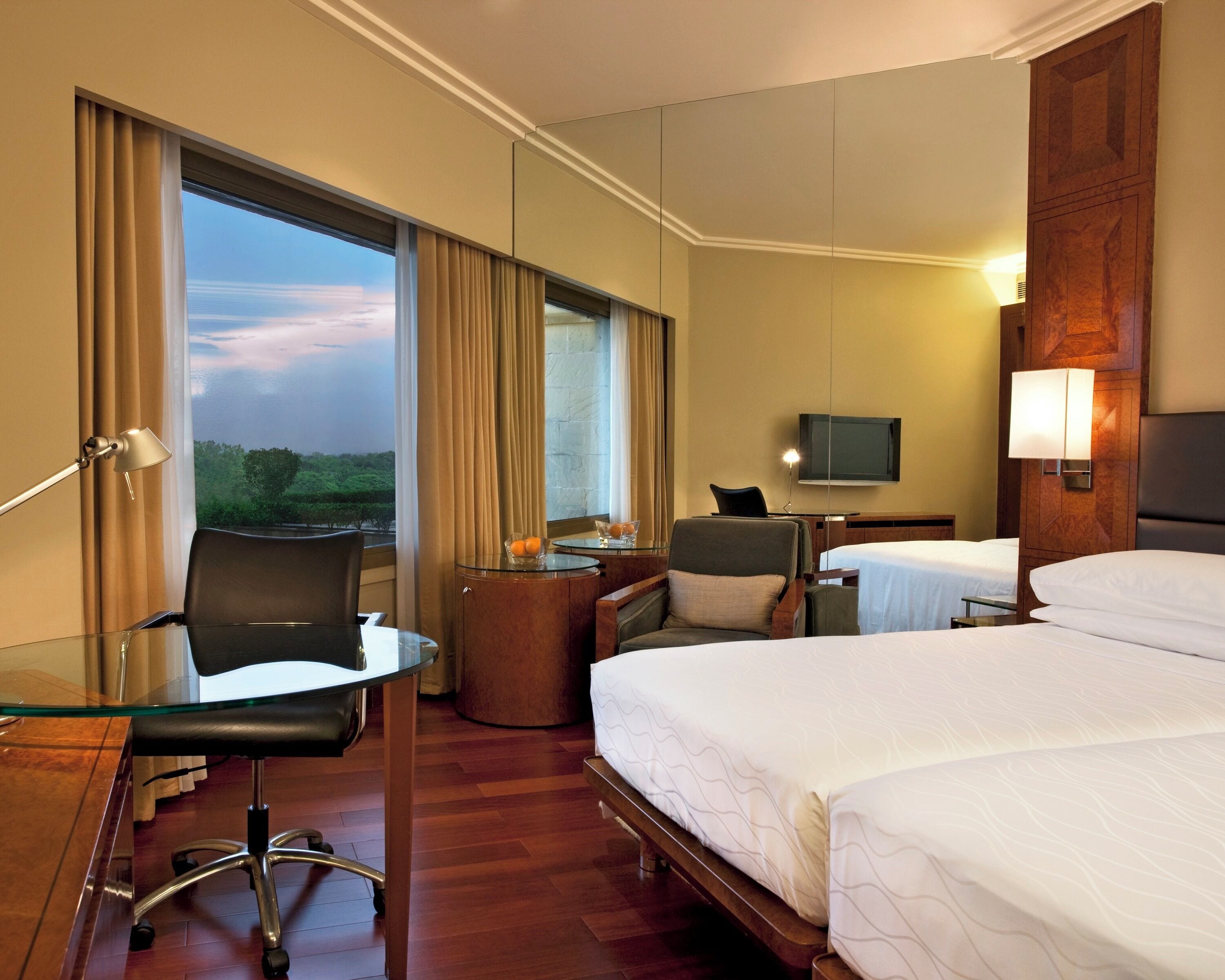 A hotel room with a bed, a desk, a chair, a TV, and a view of the outdoors.