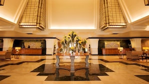 A spacious lobby with a checkered floor, a central floral arrangement, and a high ceiling with arched windows.