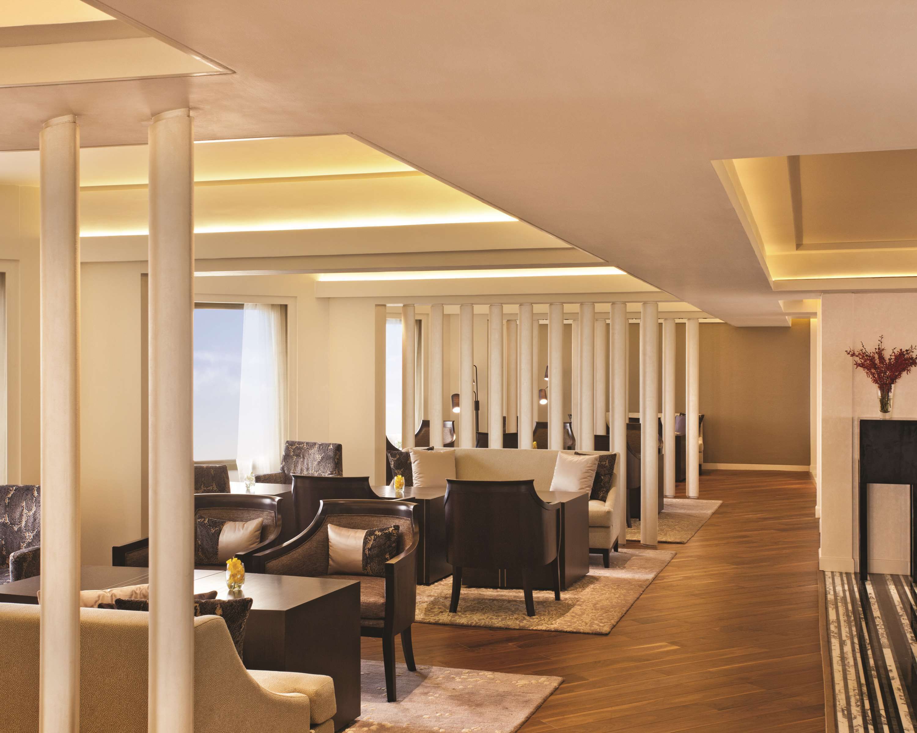 Un moderno vestíbulo de hotel con una larga recepción, varias zonas de estar con sofás y sillones, y piso de madera.