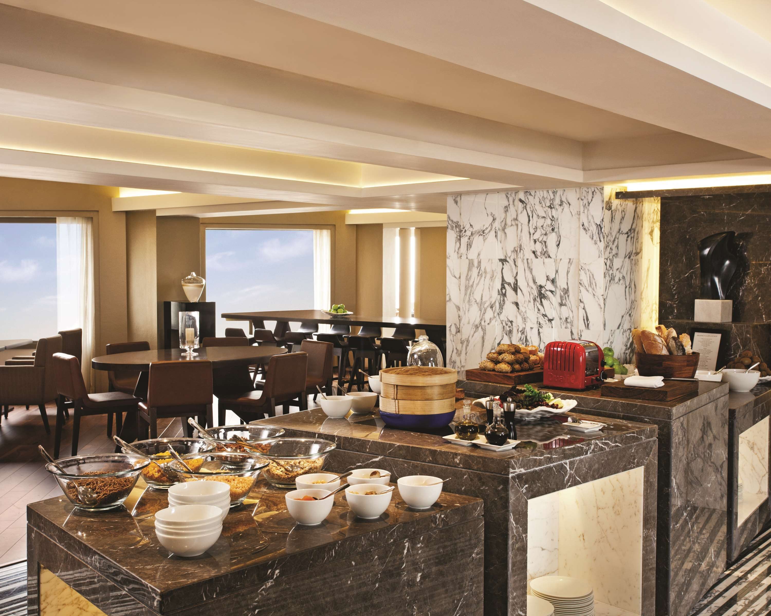 Comedor de hotel con mostradores de mármol, barra de buffet y disposición de mesas y sillas.
