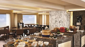 Comedor de hotel con mostradores de mármol, barra de buffet y disposición de mesas y sillas.