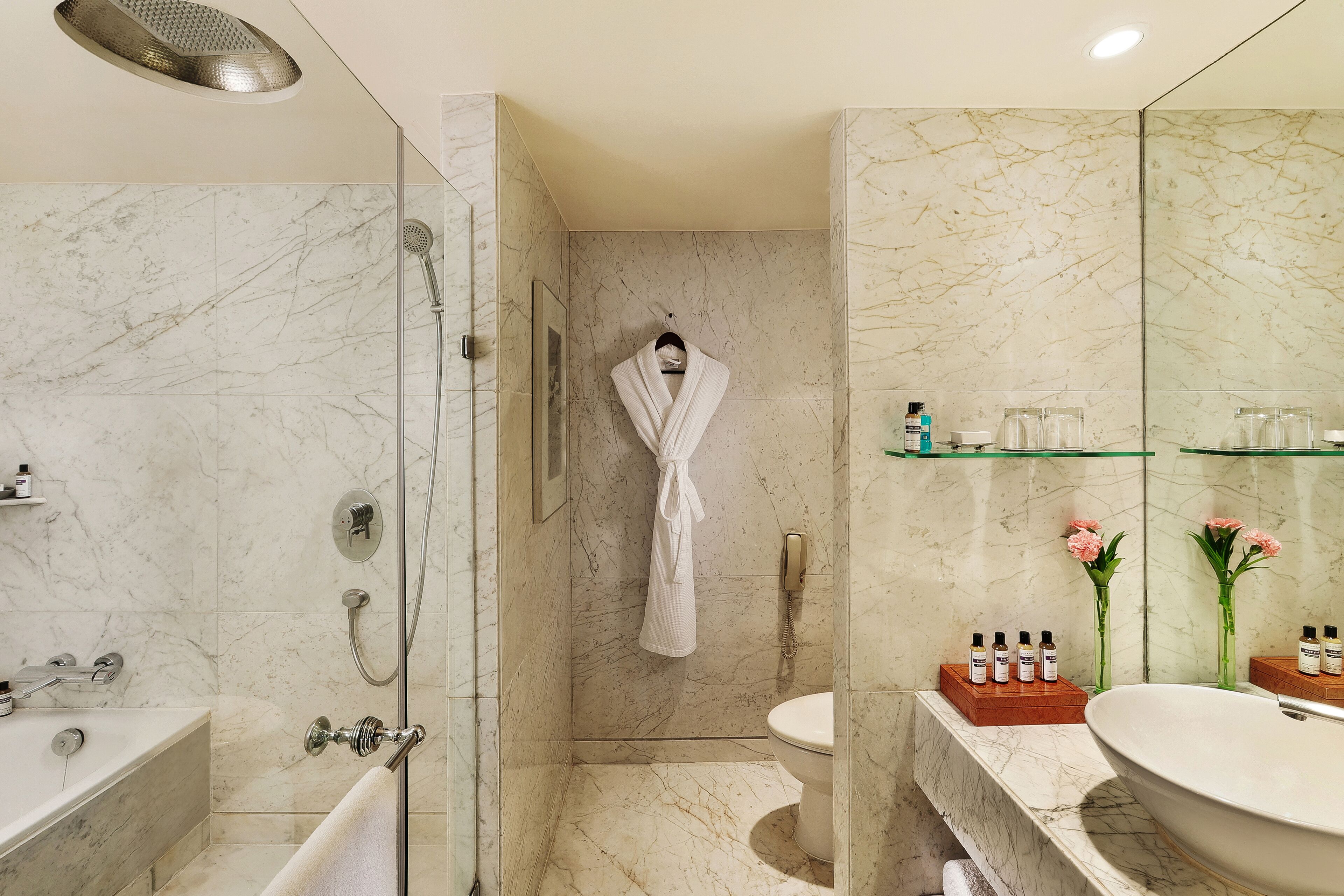 A modern bathroom with a marble shower, a bathtub, a toilet, and a large sink.