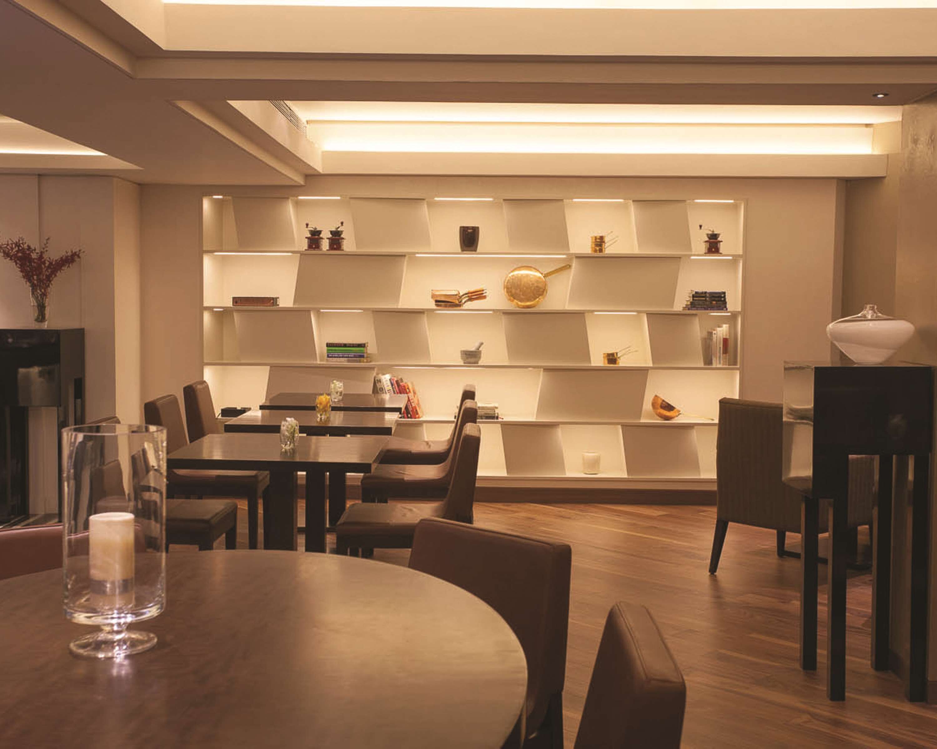 A modern dining area with a wooden table and chairs, a bookshelf with various decorative items, and a vase on the table.