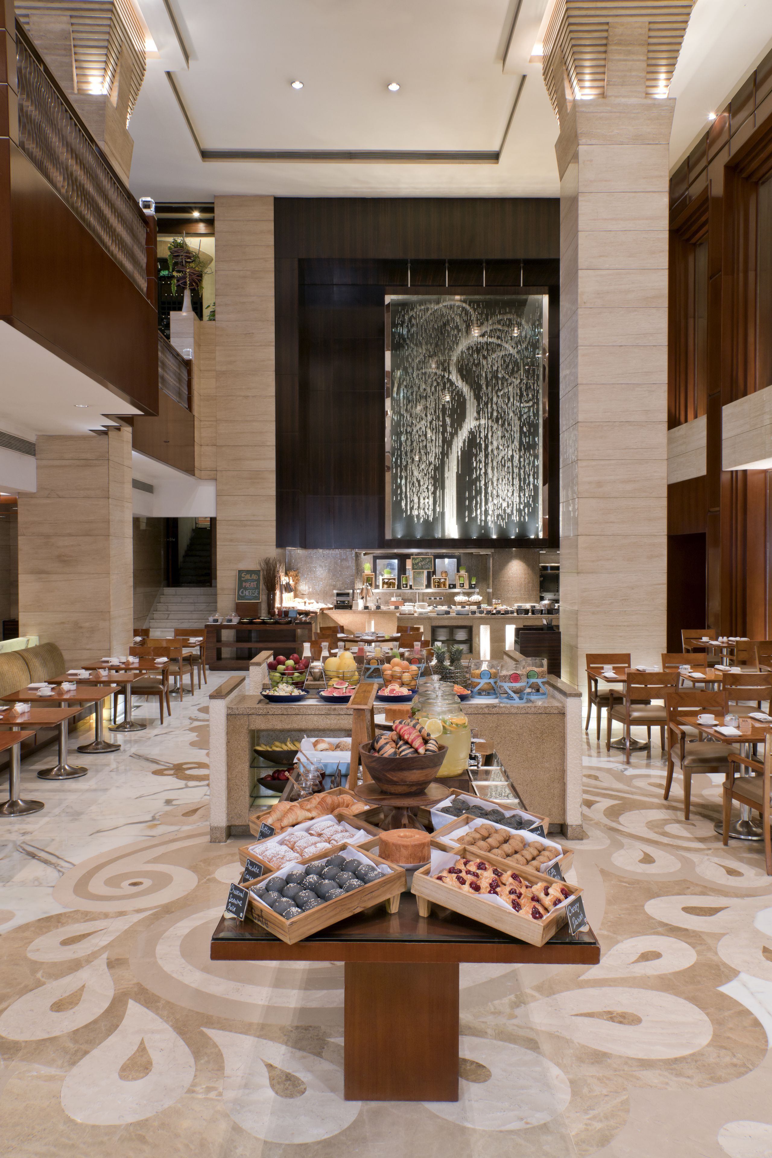 Un vestíbulo espacioso con una zona de buffet central, diversas opciones de asientos y una escalera moderna.