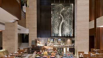 Un vestíbulo espacioso con una zona de buffet central, diversas opciones de asientos y una escalera moderna.