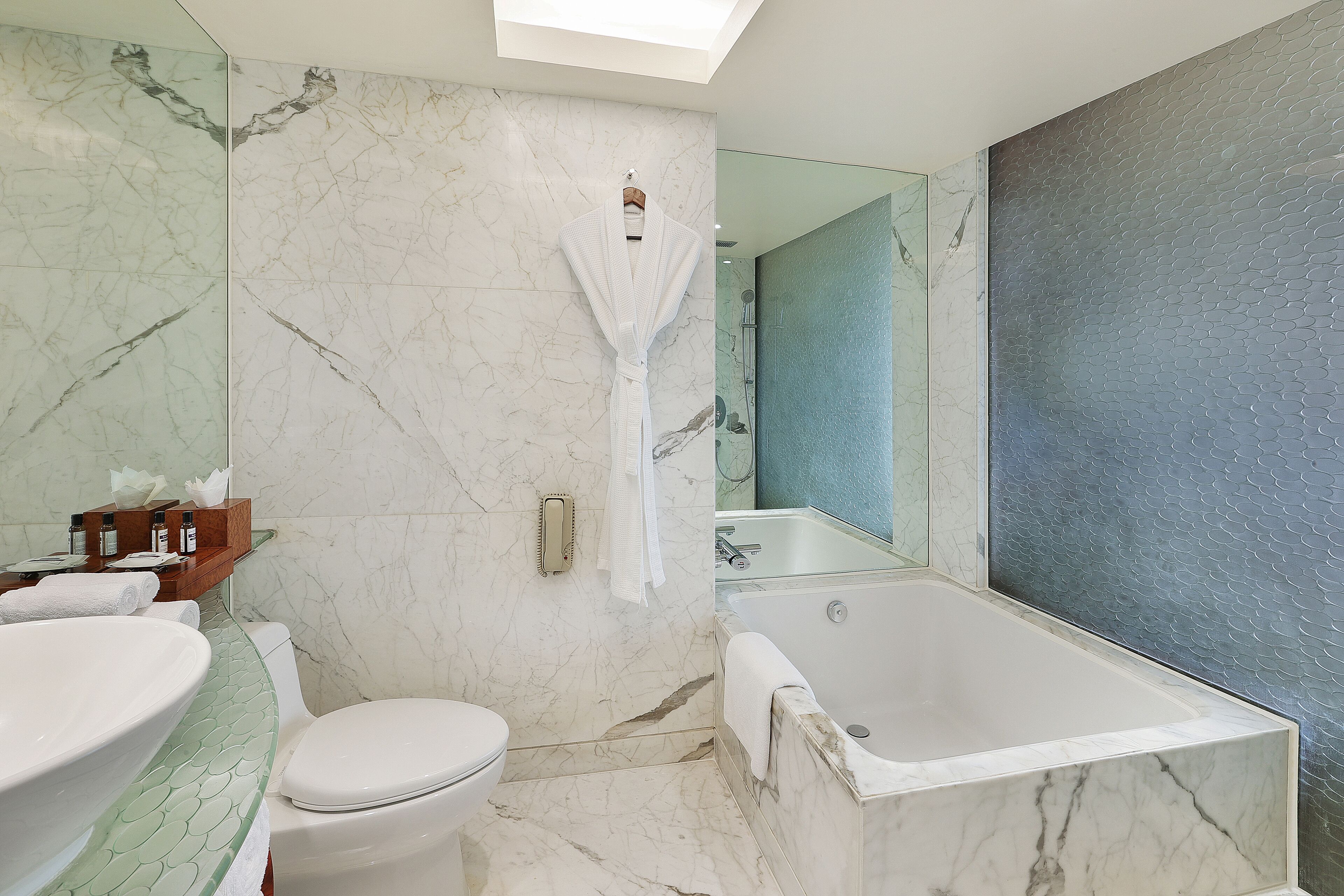A bathroom with a marble floor, a white bathtub, a toilet, and a large mirror.
