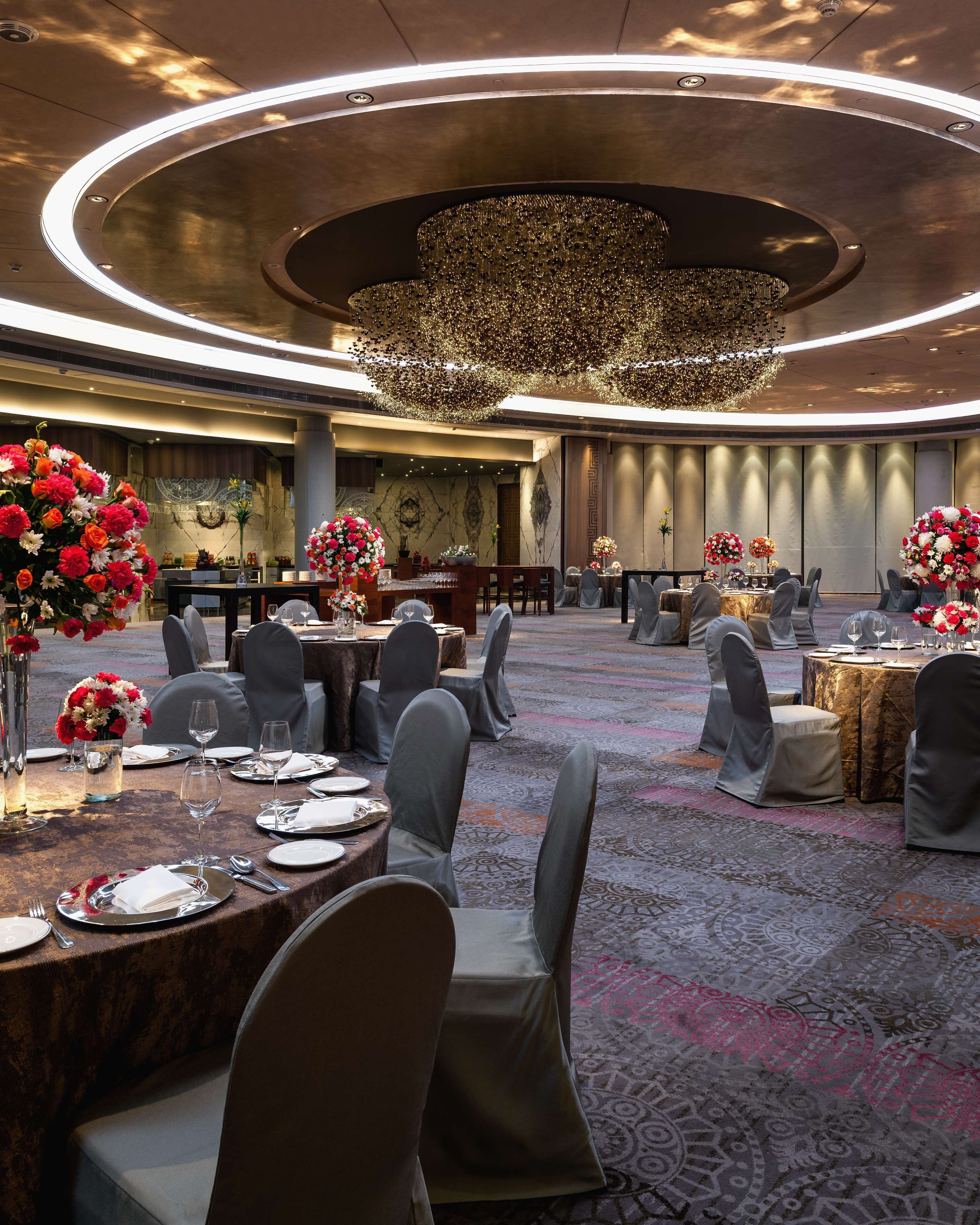 Uma sala de banquetes com mesas redondas, cadeiras cinzas e centros de mesa florais.