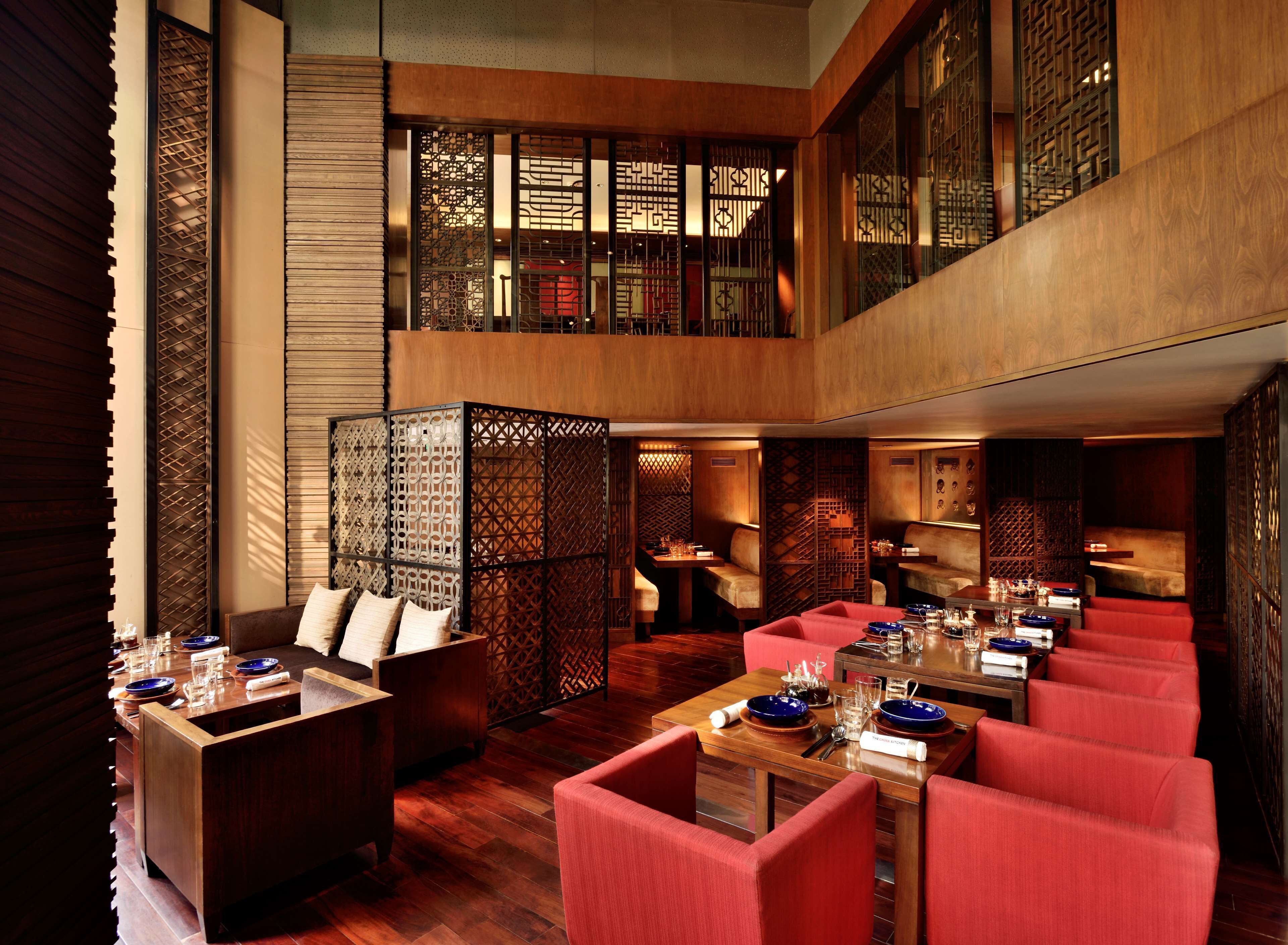 A modern restaurant with wooden flooring, red upholstered seating, and a high ceiling with decorative screens.