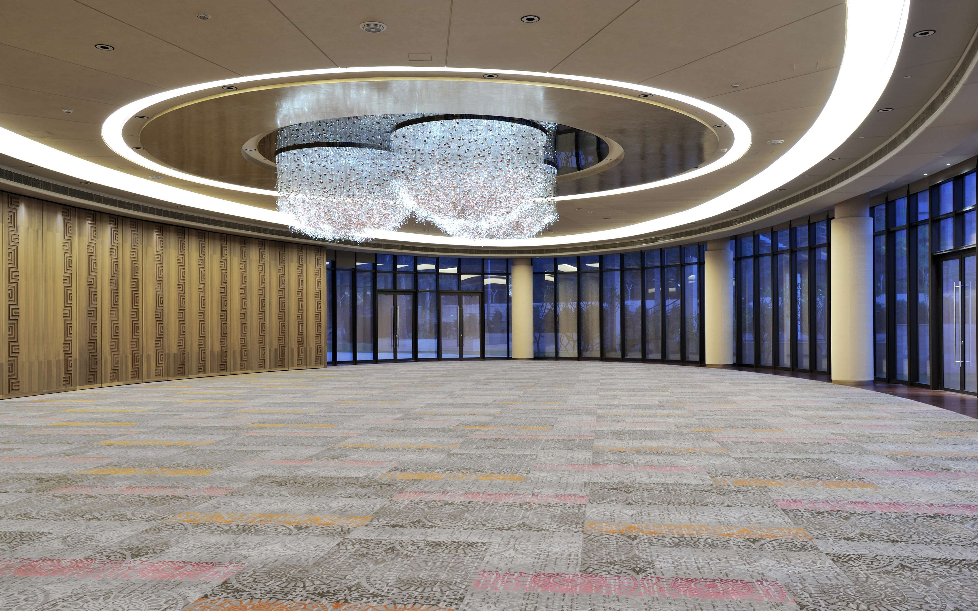 A spacious hall with a patterned carpet, large windows, and a central chandelier.