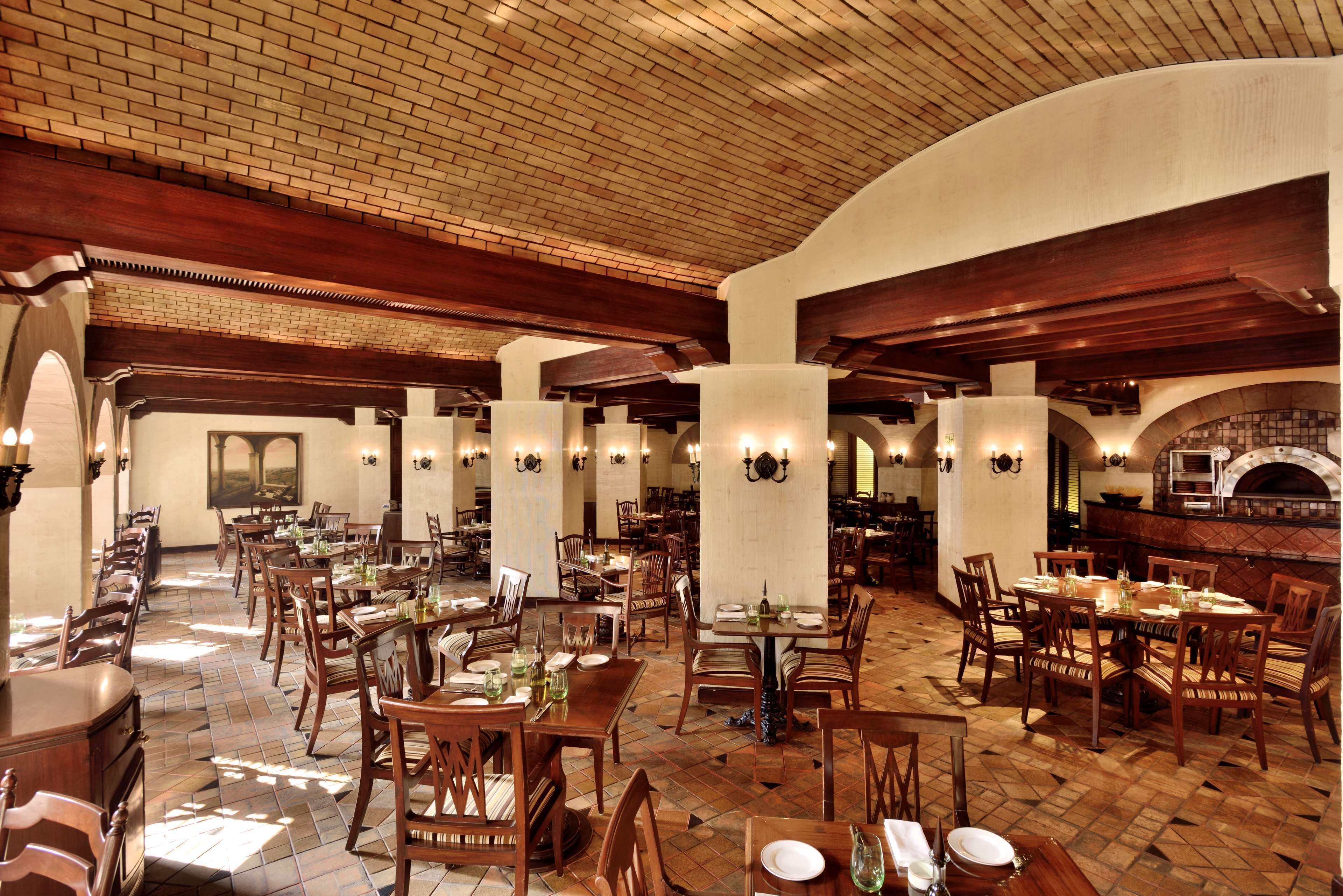 A spacious dining area with multiple tables and chairs, wooden beams on the ceiling, and a brick wall.