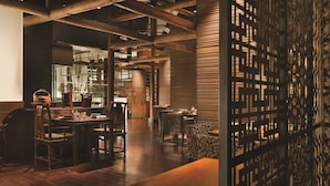 A spacious dining area with wooden tables and chairs, a large wooden ceiling, and a decorative screen with intricate patterns.