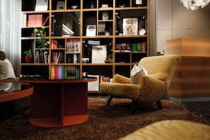A modern living room with a bookshelf, a round red table, and a patterned armchair.