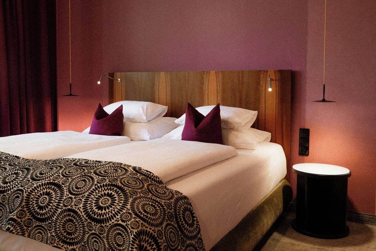 Una camera d'albergo con un letto grande, un comodino e una lampada a sospensione.
