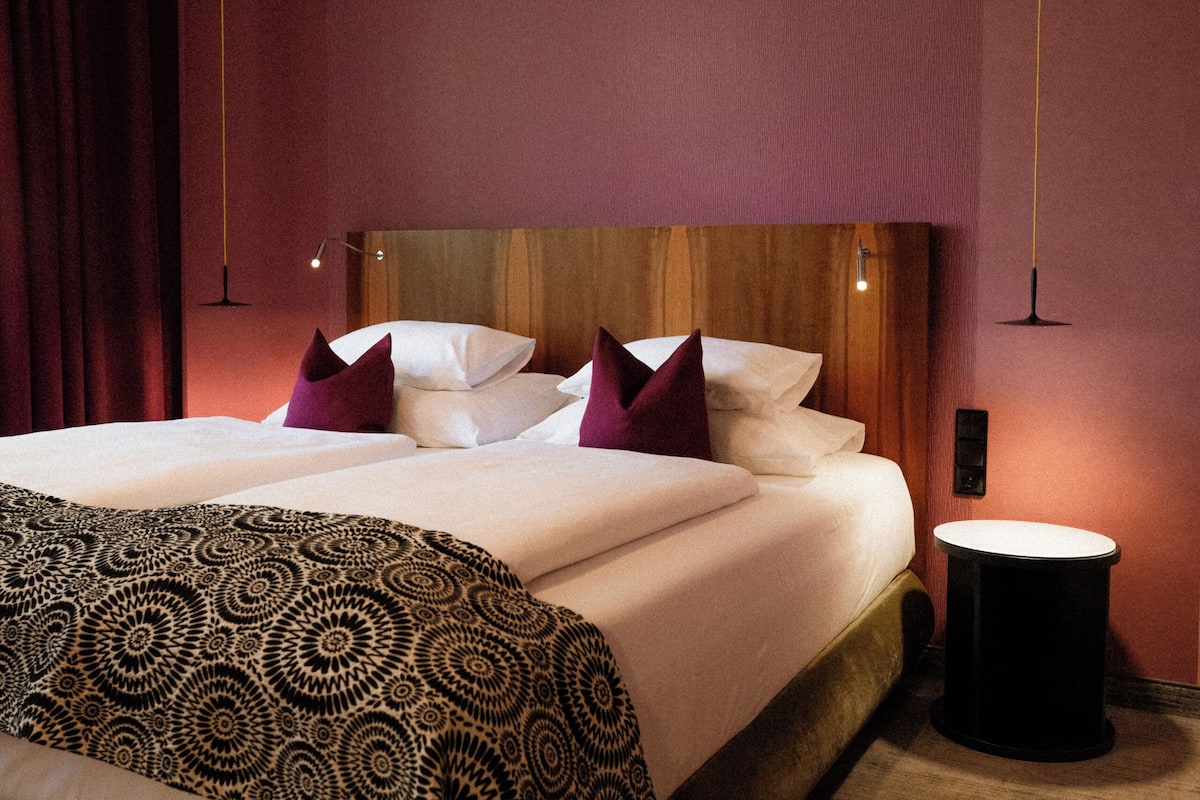 Quarto de hotel com uma cama grande, mesa de cabeceira e luminária pendente.