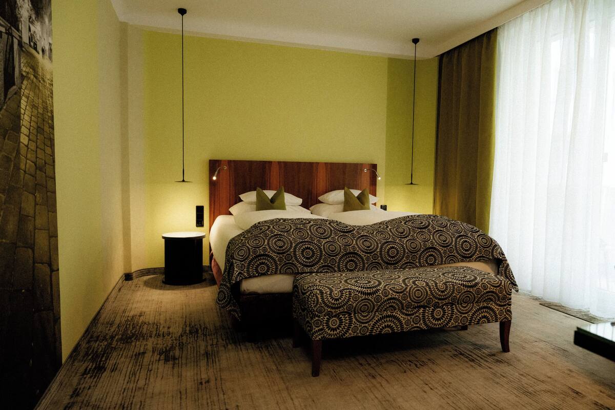 Una camera da letto con un letto, un comodino, una panca e un lampadario a parete.