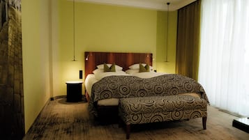 A bedroom with a bed, bedside table, bench, and a wall-mounted light fixture.