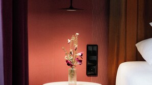 A hotel room with a bed, a round table with a vase of flowers, a wall-mounted light, and a wooden panel. - Hotel Capricorno (Vienna)